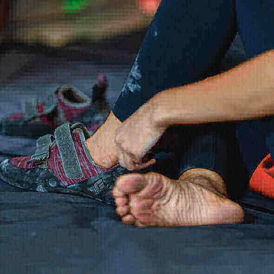 Person adjusting a barefoot shoe while sitting on the ground, showcasing the benefits of minimalist footwear for a natural walking experience.