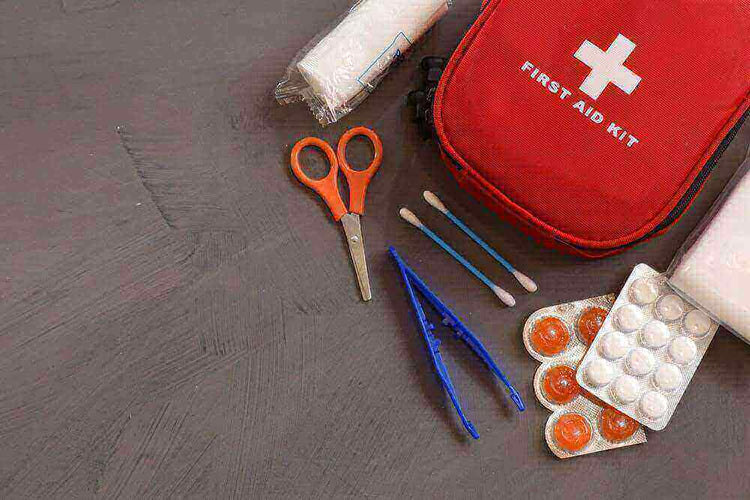 Camping first aid kit with scissors, tweezers, cotton swabs, bandages, and medication pills on a gray surface.