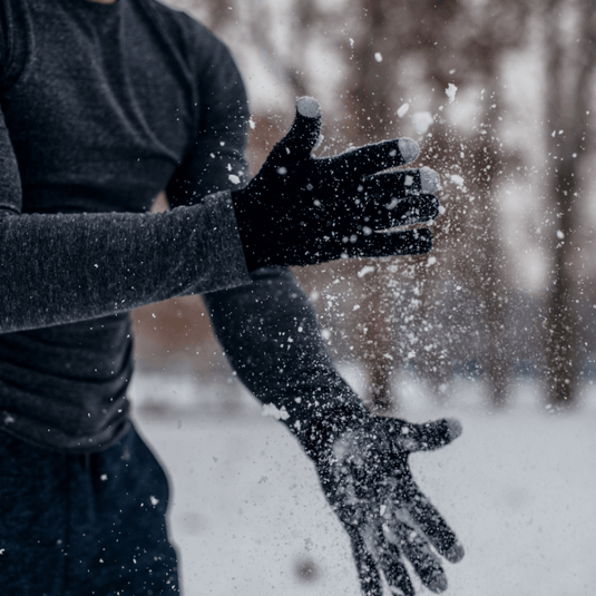 Person wearing winter gloves claps hands in snowy outdoors, showcasing warmth and natural movement.