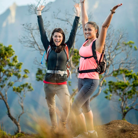 Two women in AdventureCo clothing hiking outdoors with mountains in the background.