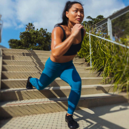 Woman training outdoors in barefoot running shoes and gym attire, enhancing foot and ankle strength with stair exercise