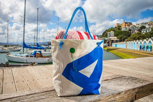 Recycled sail gear bag with blue number design, featuring durable straps and webbing, placed on a dock with boats in the background.