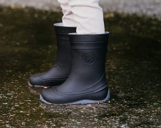 Be Lenka Kids Barefoot Rain Boots in Black worn by a child standing in a puddle, showcasing their waterproof design.
