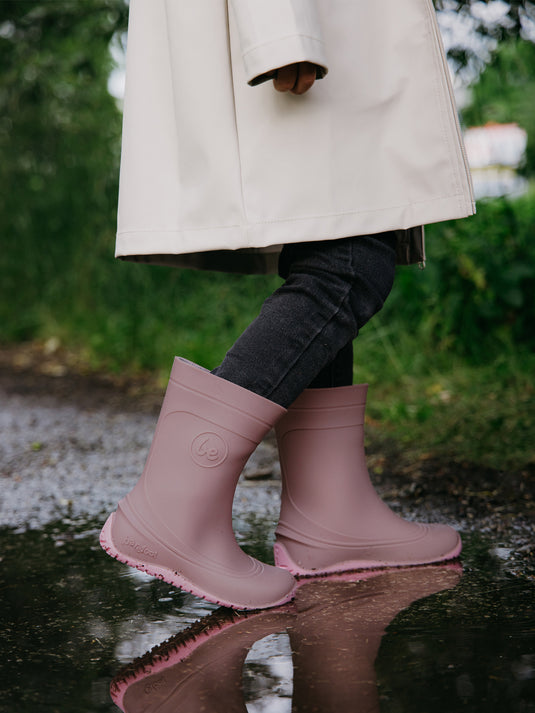 Child wearing Be Lenka Kids Barefoot Rain Boots in Misty Pink, walking through a puddle on a rainy day.
